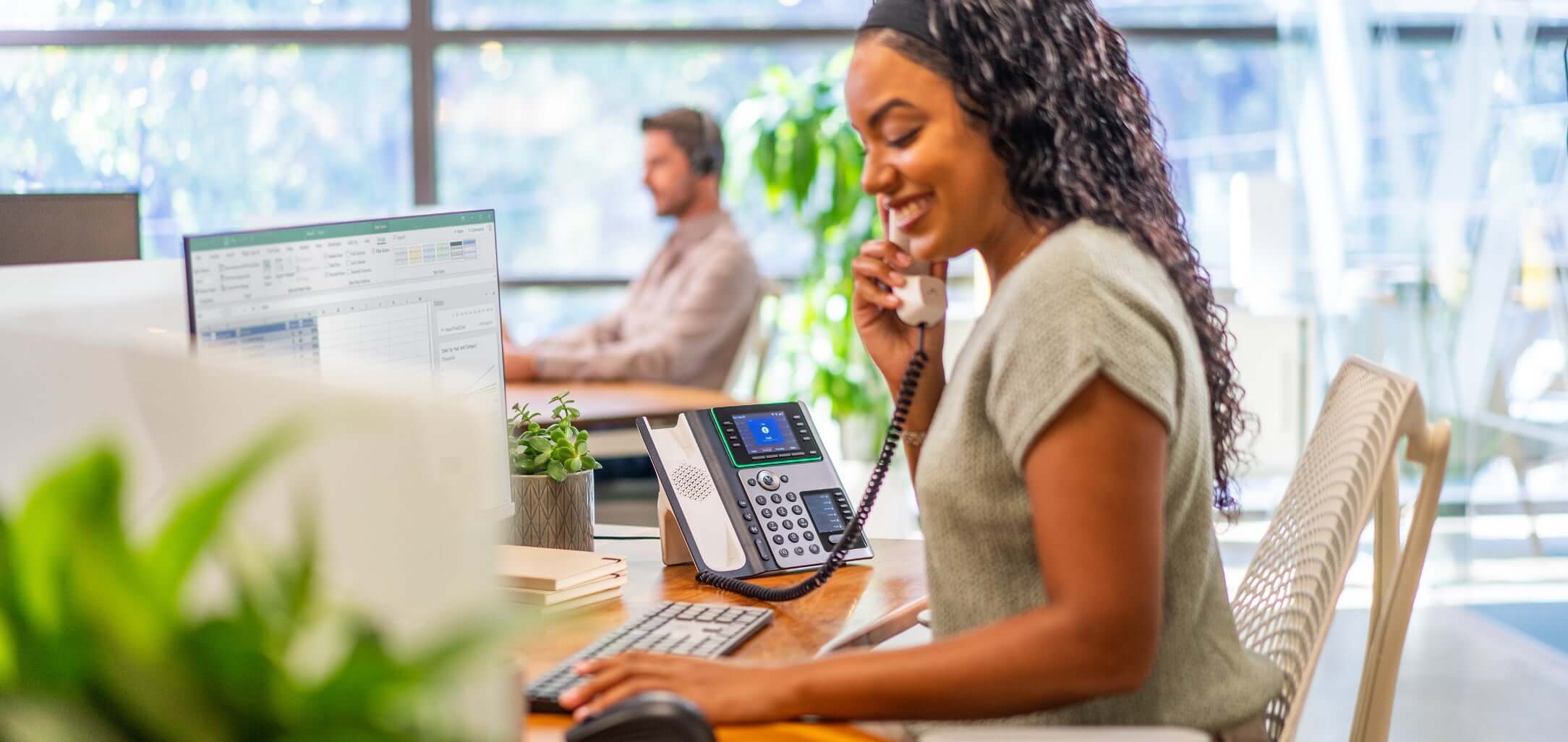 Femme assise à un bureau dans un open space, en train d’utiliser le téléphone de bureau Poly Edge E450