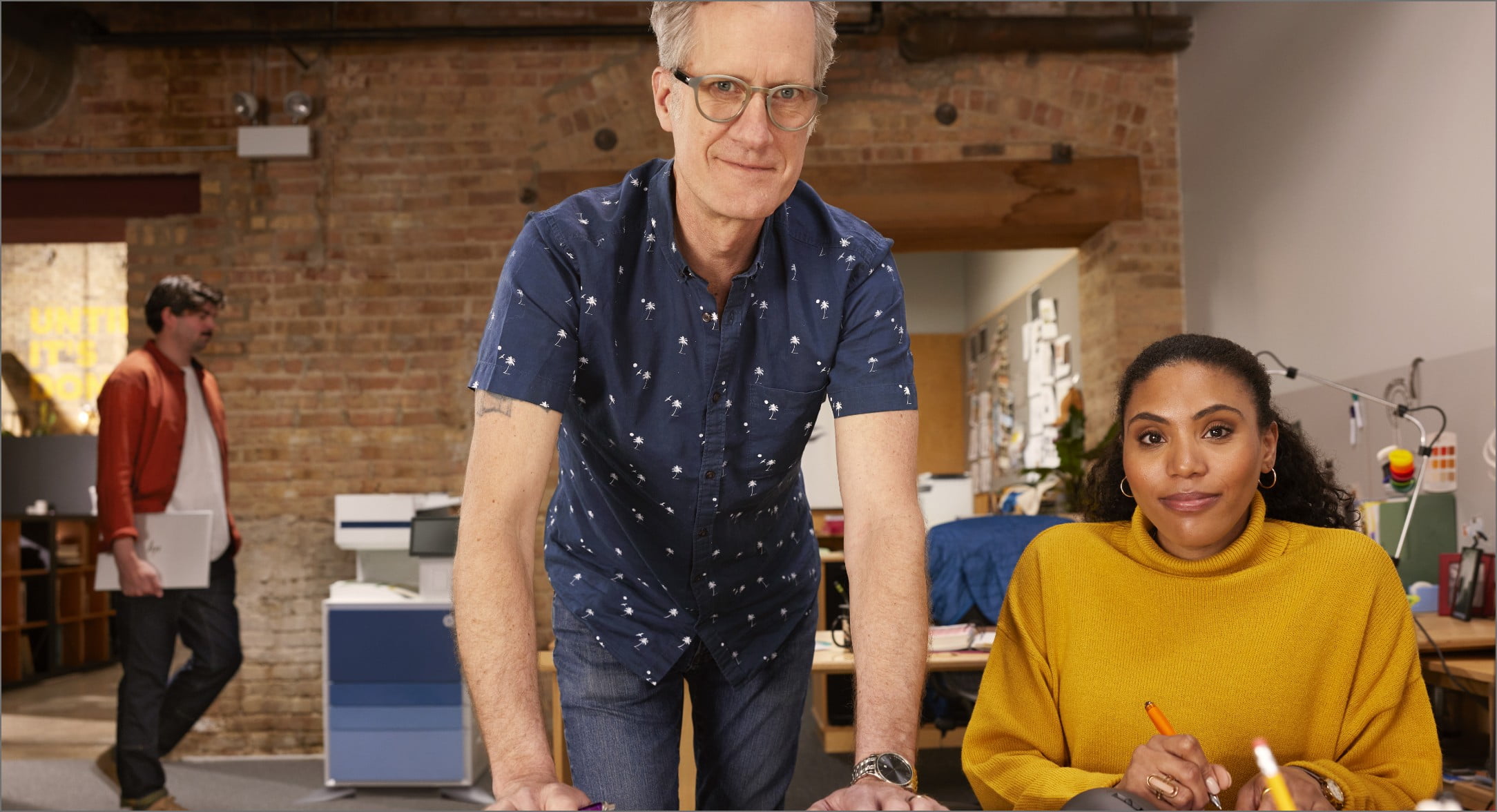 Homme debout et femme assise dans l’espace de travail d’une petite entreprise avec l’imprimante HP LaserJet Managed derrière eux